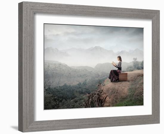 Woman Sitting On A Suitcase And Reading A Book With Landscape On The Background-olly2-Framed Art Print
