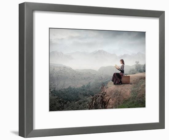 Woman Sitting On A Suitcase And Reading A Book With Landscape On The Background-olly2-Framed Art Print
