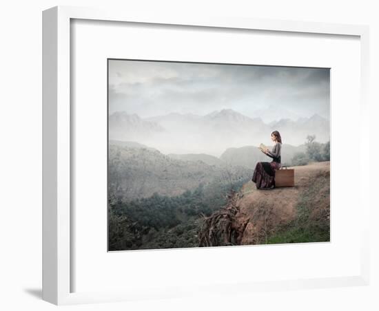 Woman Sitting On A Suitcase And Reading A Book With Landscape On The Background-olly2-Framed Art Print