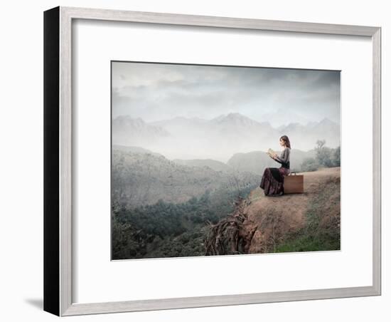 Woman Sitting On A Suitcase And Reading A Book With Landscape On The Background-olly2-Framed Art Print