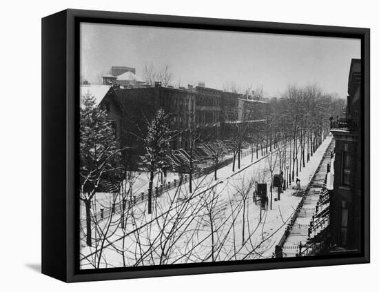 Woman sweeps snow off a snow-covered street lined with brownstones near two horse-drawn buggies.-George B^ Brainerd-Framed Premier Image Canvas