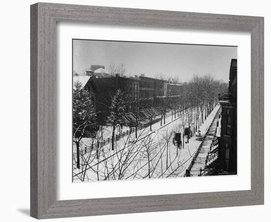 Woman sweeps snow off a snow-covered street lined with brownstones near two horse-drawn buggies.-George B^ Brainerd-Framed Photographic Print