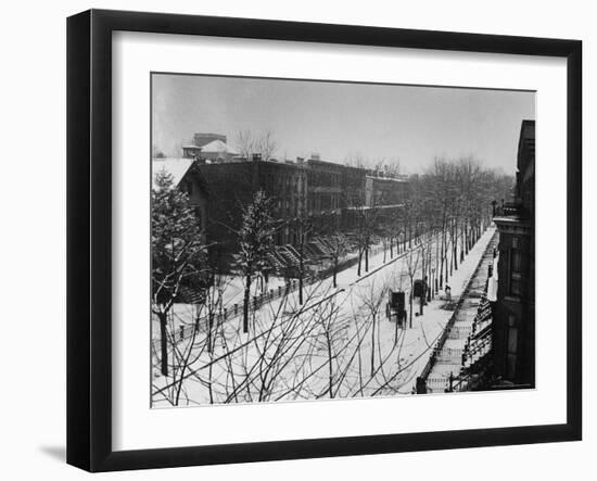 Woman sweeps snow off a snow-covered street lined with brownstones near two horse-drawn buggies.-George B^ Brainerd-Framed Photographic Print