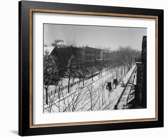 Woman sweeps snow off a snow-covered street lined with brownstones near two horse-drawn buggies.-George B^ Brainerd-Framed Photographic Print