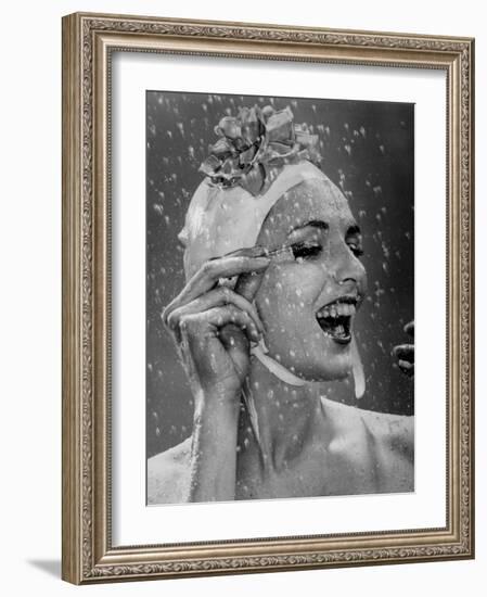 Woman Wearing Flowered Bathing Cap and Applying Mascara as Water Showers Around Her-Gjon Mili-Framed Photographic Print