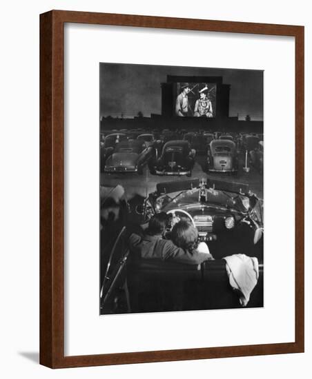 Young Couple Snuggling in Convertible as They Watch Large Screen Action at a Drive-In Movie Theater-J^ R^ Eyerman-Framed Premium Photographic Print