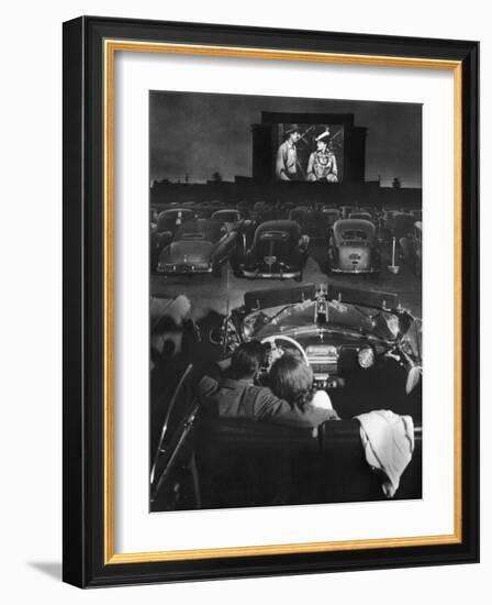Young Couple Snuggling in Convertible as They Watch Large Screen Action at a Drive-In Movie Theater-J^ R^ Eyerman-Framed Premium Photographic Print