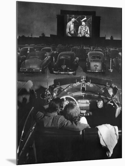 Young Couple Snuggling in Convertible as They Watch Large Screen Action at a Drive-In Movie Theater-J^ R^ Eyerman-Mounted Premium Photographic Print