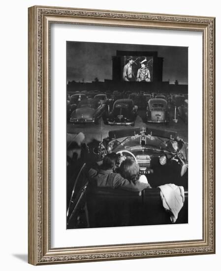 Young Couple Snuggling in Convertible as They Watch Large Screen Action at a Drive-In Movie Theater-J^ R^ Eyerman-Framed Photographic Print