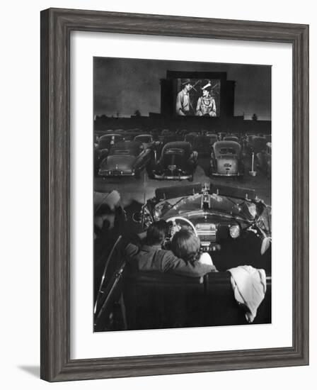 Young Couple Snuggling in Convertible as They Watch Large Screen Action at a Drive-In Movie Theater-J^ R^ Eyerman-Framed Photographic Print