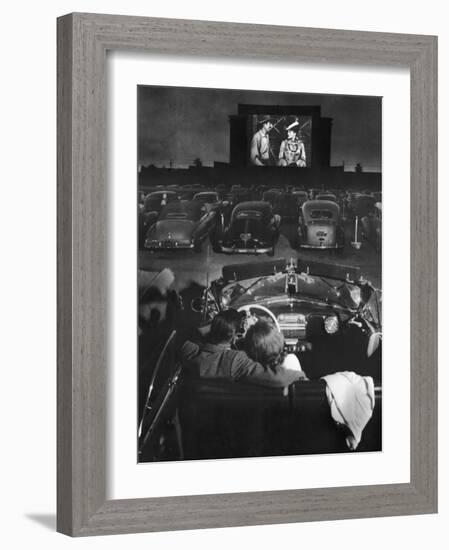 Young Couple Snuggling in Convertible as They Watch Large Screen Action at a Drive-In Movie Theater-J^ R^ Eyerman-Framed Photographic Print