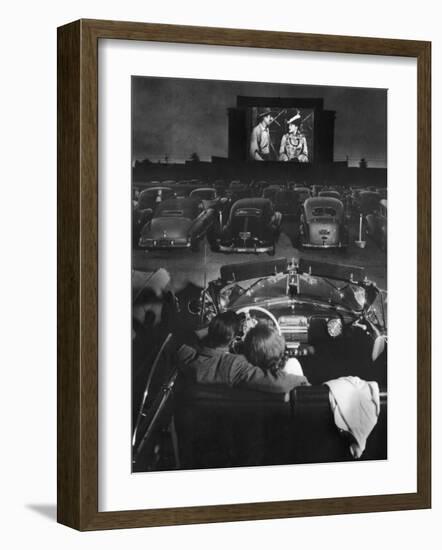 Young Couple Snuggling in Convertible as They Watch Large Screen Action at a Drive-In Movie Theater-J^ R^ Eyerman-Framed Photographic Print