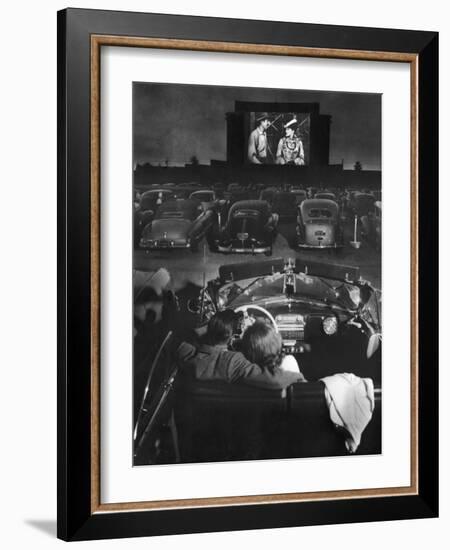 Young Couple Snuggling in Convertible as They Watch Large Screen Action at a Drive-In Movie Theater-J^ R^ Eyerman-Framed Photographic Print