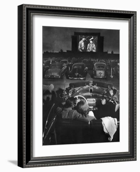 Young Couple Snuggling in Convertible as They Watch Large Screen Action at a Drive-In Movie Theater-J^ R^ Eyerman-Framed Photographic Print