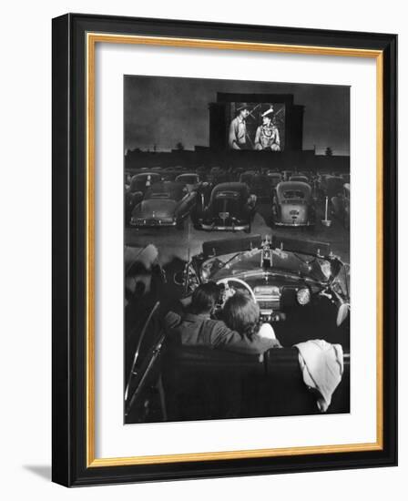 Young Couple Snuggling in Convertible as They Watch Large Screen Action at a Drive-In Movie Theater-J^ R^ Eyerman-Framed Photographic Print