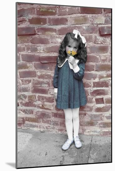 Young Girl Standing in Front of a Stone Wall Smelling a Flower.-Nora Hernandez-Mounted Giclee Print