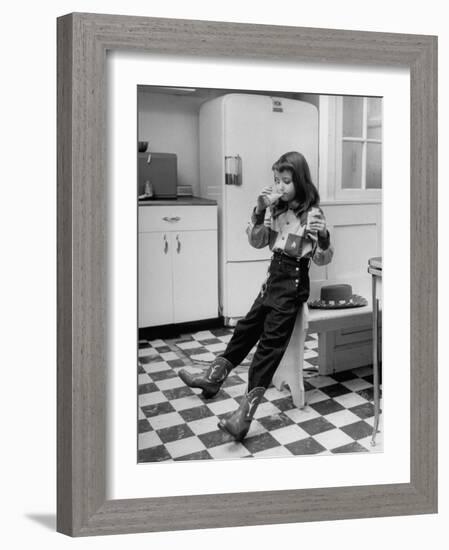 Young Girl Wearing Cowgirl Outfit Drinking Milk and Eating Sandwich in Kitchen-Nina Leen-Framed Photographic Print