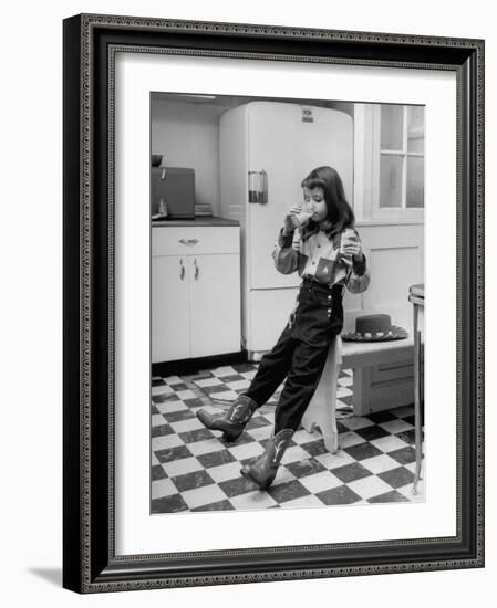 Young Girl Wearing Cowgirl Outfit Drinking Milk and Eating Sandwich in Kitchen-Nina Leen-Framed Photographic Print