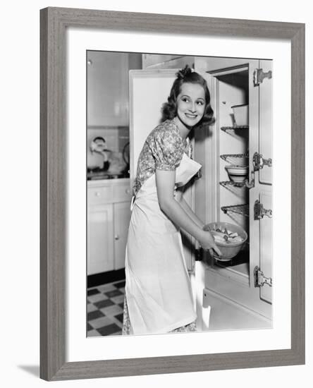 Young Woman in an Apron in Her Kitchen Taking Food Out of the Refrigerator-null-Framed Photo