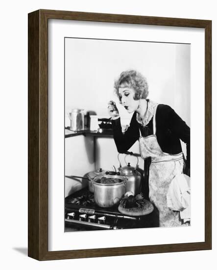 Young Woman in an Apron in Her Kitchen Tasting Her Food from a Pot-null-Framed Photo