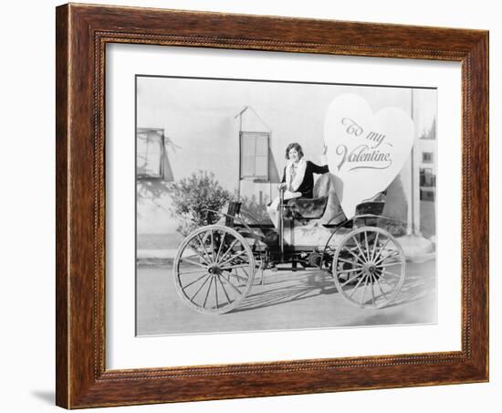 Young Woman Sitting on a Car Holding a Big Heart Shaped Sign-null-Framed Photo