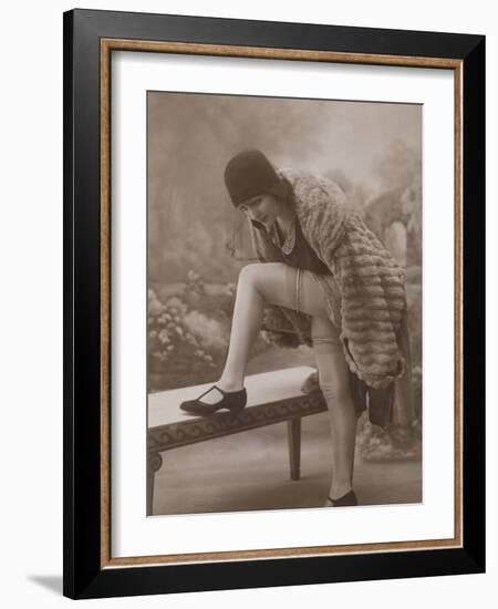 Young Woman Wearing a Fur Coat Cloche Hat and T-Bar Shoes Lifts Her Leg Up-null-Framed Photographic Print