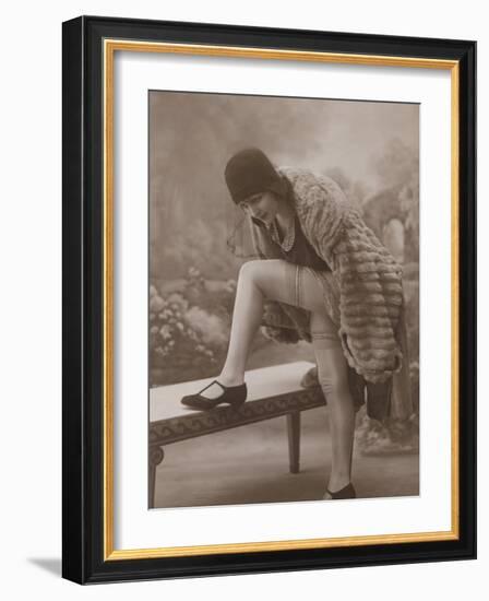 Young Woman Wearing a Fur Coat Cloche Hat and T-Bar Shoes Lifts Her Leg Up-null-Framed Photographic Print